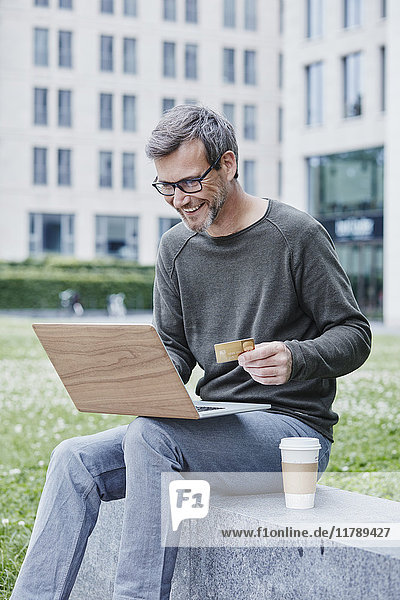 Erwachsener Mann im Freien mit Laptop,  Kreditkarte und Kaffee zum Mitnehmen
