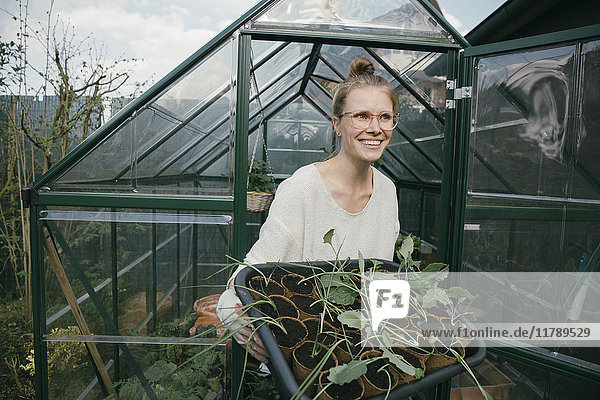 Porträt einer glücklichen jungen Frau mit Topfpflanzen vor dem Gewächshaus