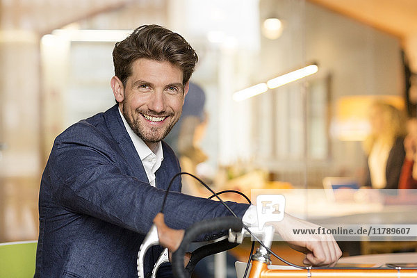 Ein junger Geschäftsmann im Büro  der sich auf sein Rennrad stützt.