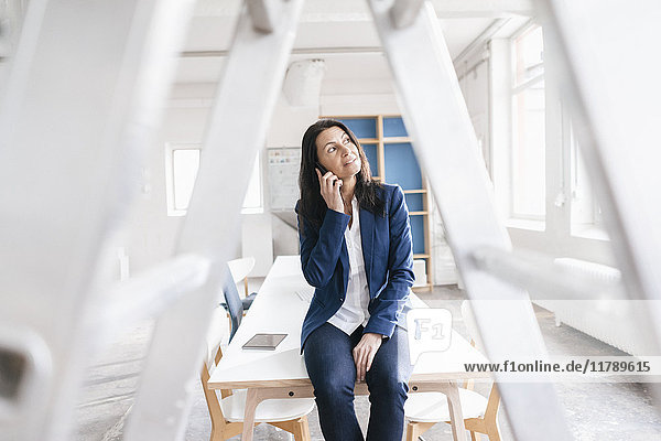 Geschäftsfrau am Telefon sitzt auf dem Schreibtisch in einem Loft