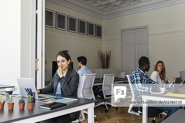 Young businesswoman using laptop  colleagues working in background