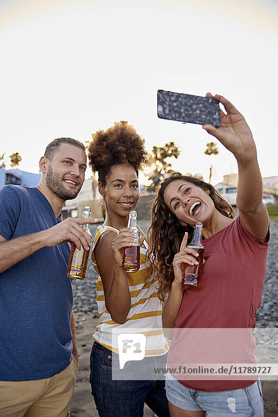 Three friends with beer bottles taking selfie on the beach