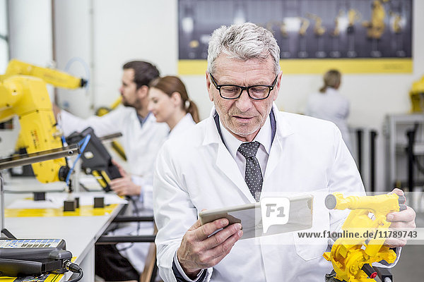 Ingenieur hält Tablette und Modell eines Industrieroboters