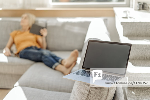 Laptop auf Couch mit Frau im Hintergrund