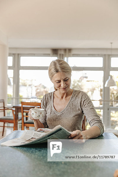 Woman at home sitting at table with cup of coffee and newspaper