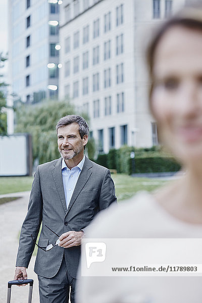 Smiling businesswoman outdoors with laptop and businessman in background