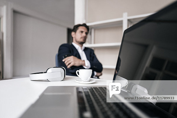 Laptop  Kopfhörer  Kaffeetasse und Geschäftsmann im Hintergrund