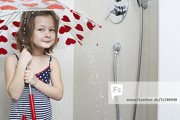Portrait of smiling little girl taking shower with umbrella