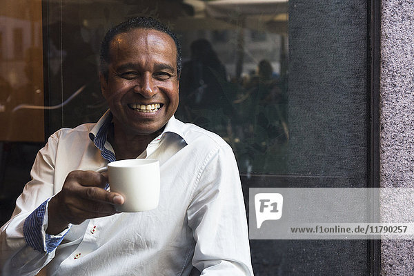Porträt des lachenden Mannes in einem Café mit Tasse Kaffee