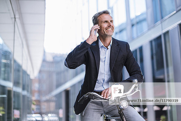 Smiling businessman with bicycle on cell phone in the city