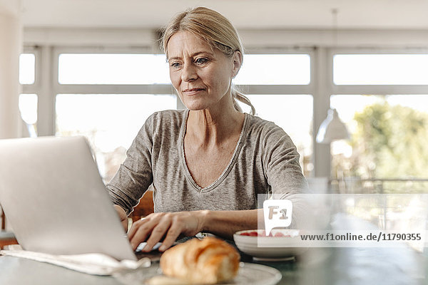 Woman at home having breakfast and using laptop