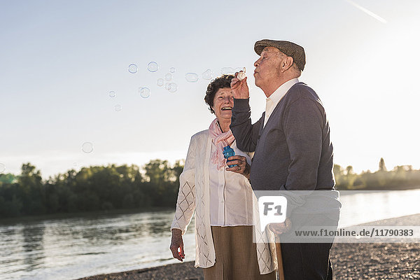Senior Mann  der bei Sonnenuntergang Seifenblasen am Strand bläst.
