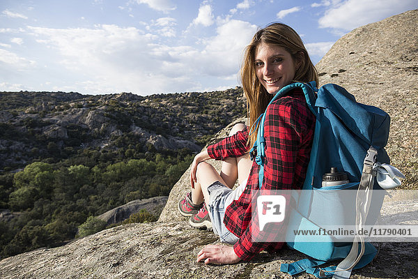 Spanien  Madrid  lächelnde junge Frau auf einem Felsen während eines Trekkingtages