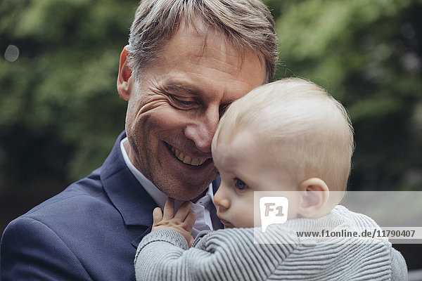 Happy mature businessman holding baby boy outdoors