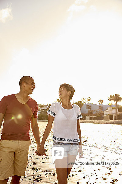 Ein verliebtes Paar geht Hand in Hand am Strand spazieren.