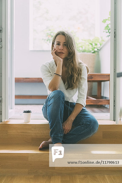 Junge Frau mit Kaffee zum Mitnehmen sitzend auf dem Balkon
