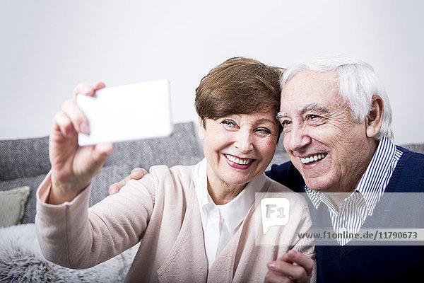 Senior Paar sitzt auf der Couch und nimmt sich ein Smartphone Selfie