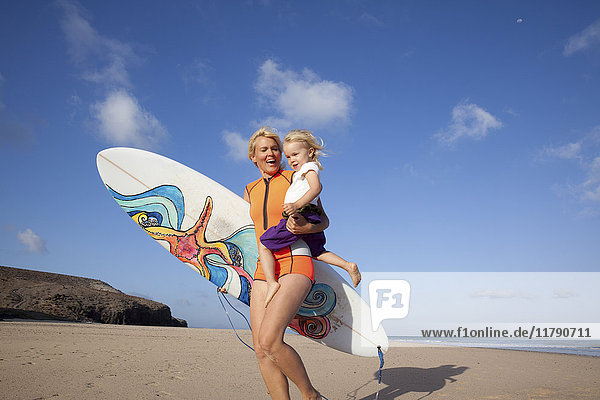 Spanien  Fuerteventura  glückliche Mutter und Tochter beim Spaziergang mit Surfbrett am Strand