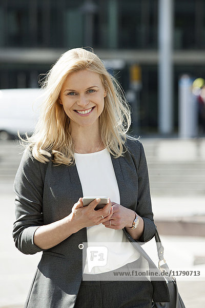 Portrait of smiling blond businesswoman with cell phone and handbag