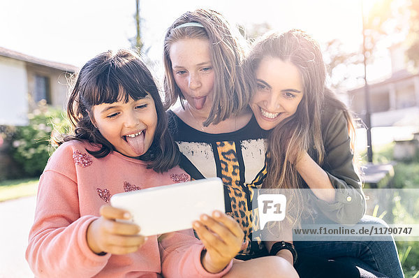 Drei verspielte Mädchen mit einem Selfie im Freien