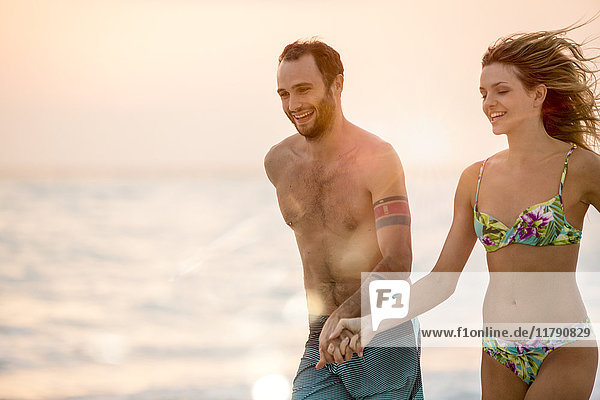 Ein junges Paar  das am Strand rennt und Händchen hält.