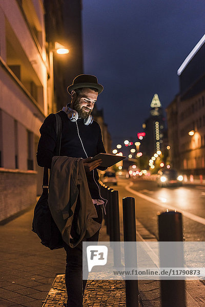 Stylish young man with tablet on urban street at night