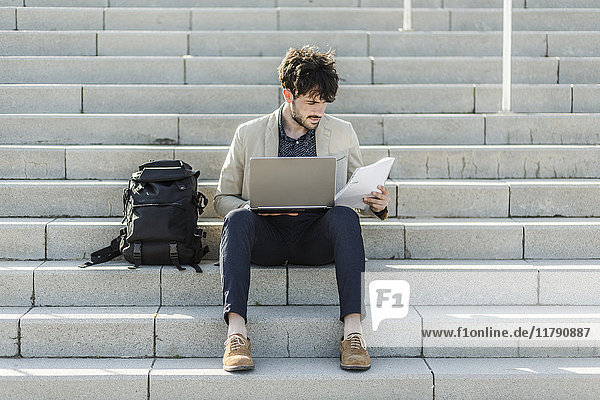 Pensive man with laptop sitting on steps checking documents