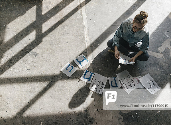 Junge Frau auf Betonboden sitzend  auf Briefvorlagen arbeitend