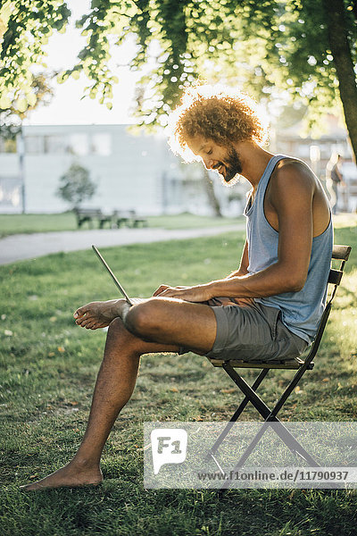 Man with beard and curly hair using laptop in park