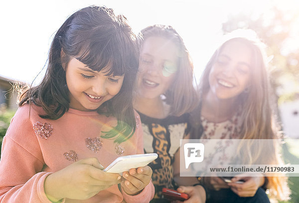 Drei glückliche Mädchen mit ihren Smartphones im Freien