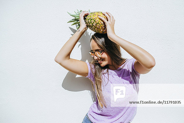Happy young woman holding pineapple in front of white wall