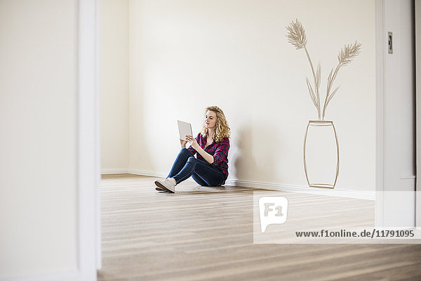 Junge Frau im neuen Zuhause sitzt auf dem Boden mit Tablette