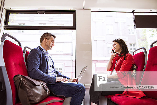 Geschäftsmann und Frau mit Laptop und Smartphone im Bus