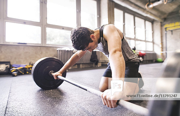 Young athlete exercising with barbell in gym