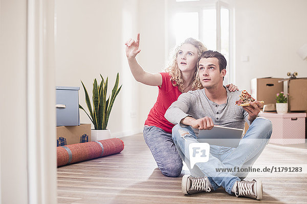 Junges Paar in neuem Zuhause sitzend auf dem Boden mit Tablette