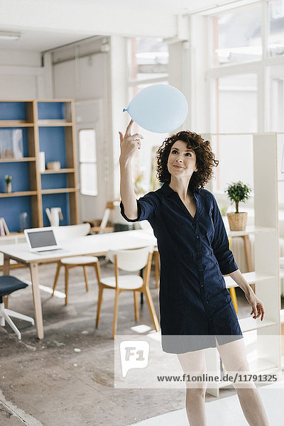 Businesswoman in office balancing balloon on finger
