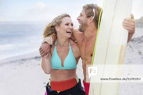 Lachendes Paar am Strand mit Surfbrett