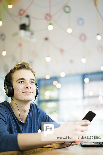 Porträt eines entspannten jungen Mannes beim Musikhören mit Kopfhörer und Smartphone im Café