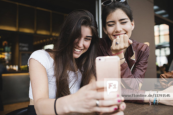 Zwei glückliche junge Frauen  die das Handy in einer Bar anschauen.