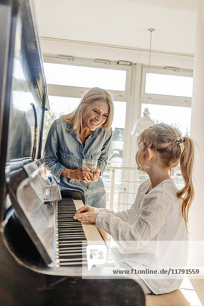 Fröhliche reife Frau  die das Mädchen am Klavier ansieht.