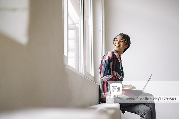 Lächelnde Frau am Fenster sitzend mit Laptop