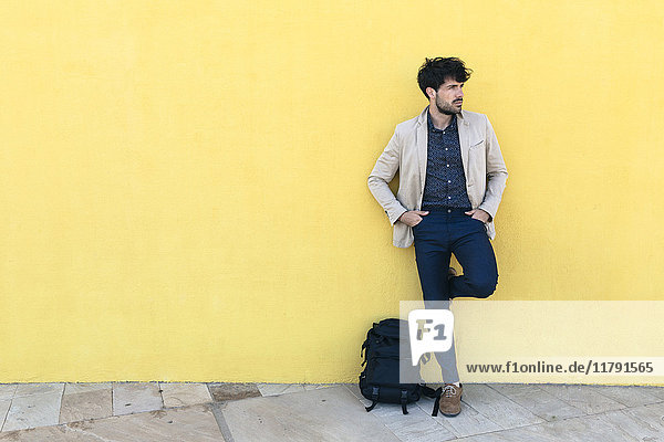 Junger Mann mit Rucksack vor gelber Wand stehend