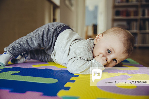 Porträt des kleinen Jungen mit dem Finger im Mund auf dem Boden im Wohnzimmer.