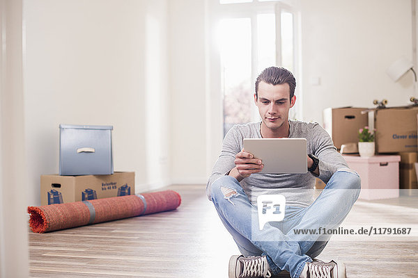 Young man in new home sitting on floor with tablet