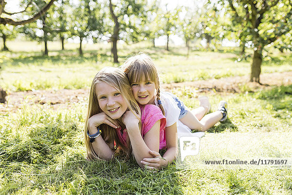 Two smiling sisters lying on meadow