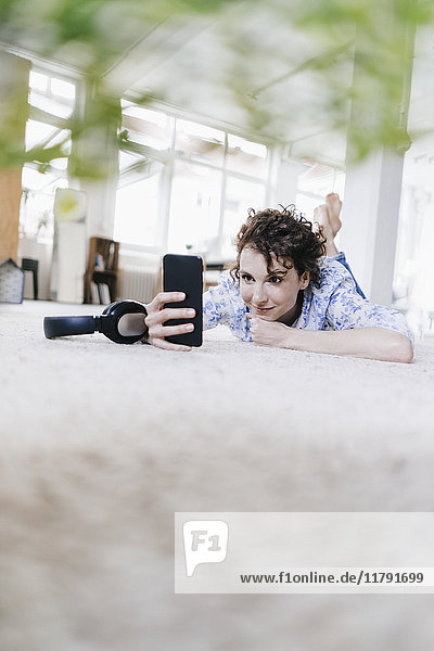 Frau liegt auf dem Boden in ihrer Wohnung  mit Smartphone