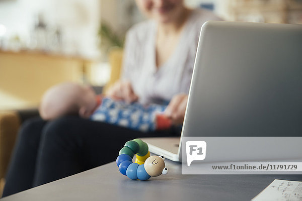 Baby toy next to laptop of mother holding her newborn baby at home