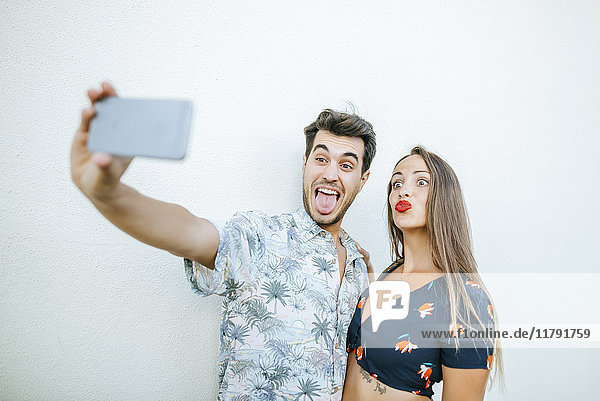 Verspieltes Paar  das einen Selfie mit Smartphone vor der weißen Wand nimmt.