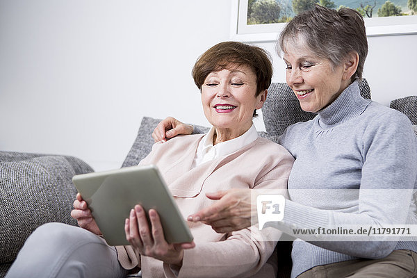 Zwei ältere Frauen sitzen auf der Couch und schauen auf das digitale Tablett.