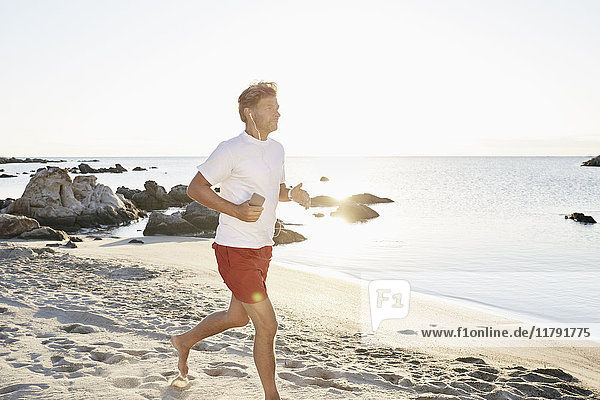 Reife Männer joggen am Strand beim Musikhören mit Smartphone und Kopfhörer